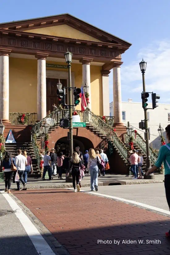 A columned,, two-story, building welcomes shoppers with an inviting staircase and ararch.